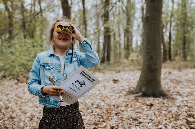 Ein Mädchen schaut durch ein Fernglas im Wald in Drenthe.