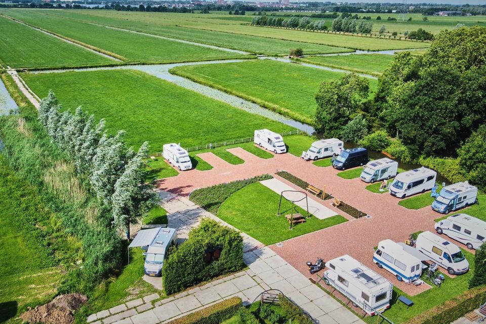Luchtfoto van een camperplaats midden in het groene polderlandschap met meerdere campers geparkeerd op verharde plaatsen.