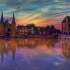 Foto van de Waterpoort in Sneek bij avondlicht, de lucht kleurt blauw, geel en roze, het water paars.