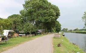 Een rustig laantje op Camping De Boogaard in Oudewater, met kampeerplekken en tenten langs het water, omgeven door groen en bomen.