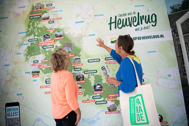Twee vrouwen staan voor een grote kaart van de regio De Utrechtse Heuvelrug. De kaart is groen en ze wijzen naar de kaart.