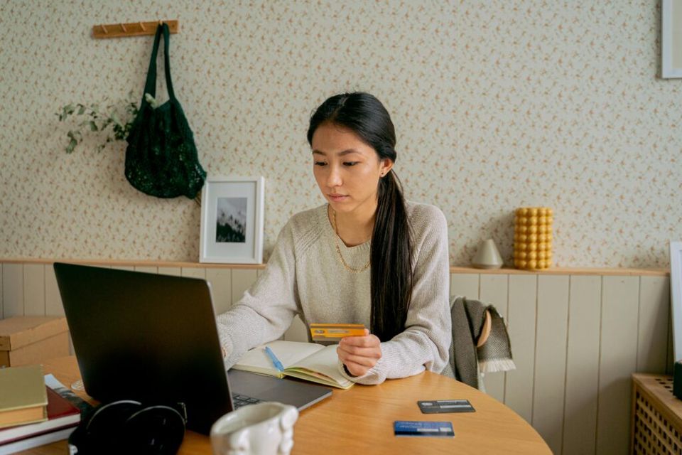 Een vrouw zit achter haar laptop met drie bankpassen op tafel