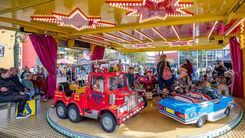Kinderen zitten in een blauwe en rode auto in de draaimolen op de Kinderkermis in Hilversum.