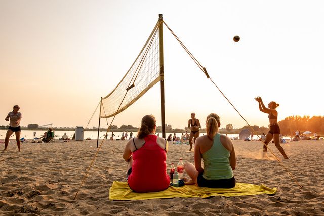 Strand met mensen die aan het volleyballen zijn en op het strand liggen.