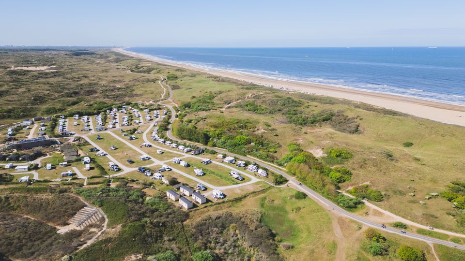 Dronebeeld van Strandcamping Zuidduinen in Katwijk aan Zee. Campers en caravans staan midden in de weidse duinen van Nationaal Park Hollandse Duinen en met de Noordzee en het zandstrand in beeld.
