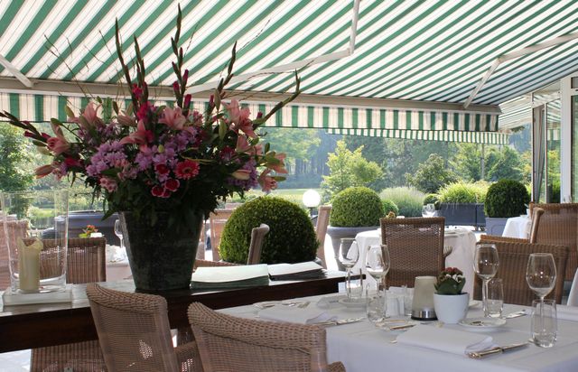 Terras onder groen-witte luifel met ingedekte tafels en een groot bloemstuk.