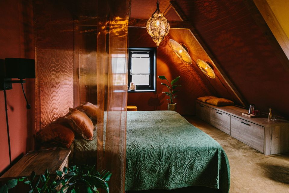 Een hotelkamer in warme kleuren rood en groen.