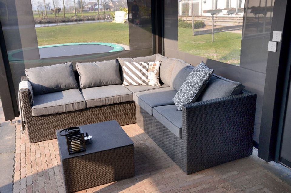 Overdekt terras en lounge van B&B Aan de Hollandse IJssel in Montfoort met comfortabele banken en uitzicht op de tuin met trampoline en het water.