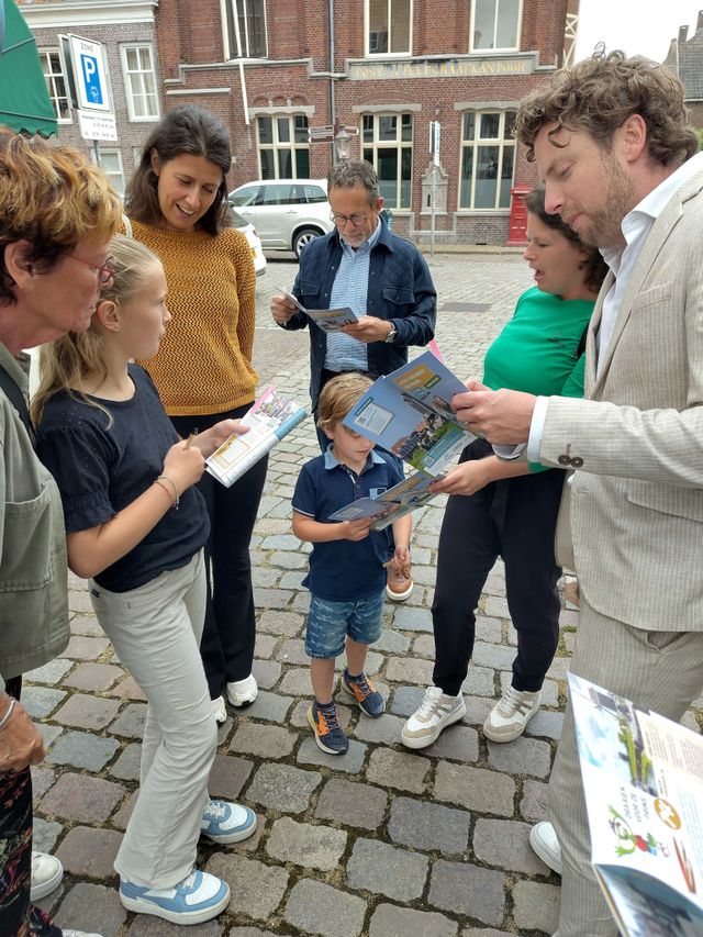 Een groep volwassenen en kinderen is druk in de weer met het opdrachtenboekje van de spreekwoordenroute.