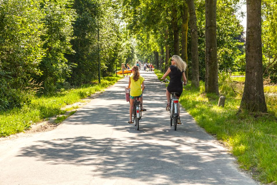 Twee vrouwen fietsen op een zonnige zomerdag door het groene buitengebied van Woerden, omringd door bomen en natuur.