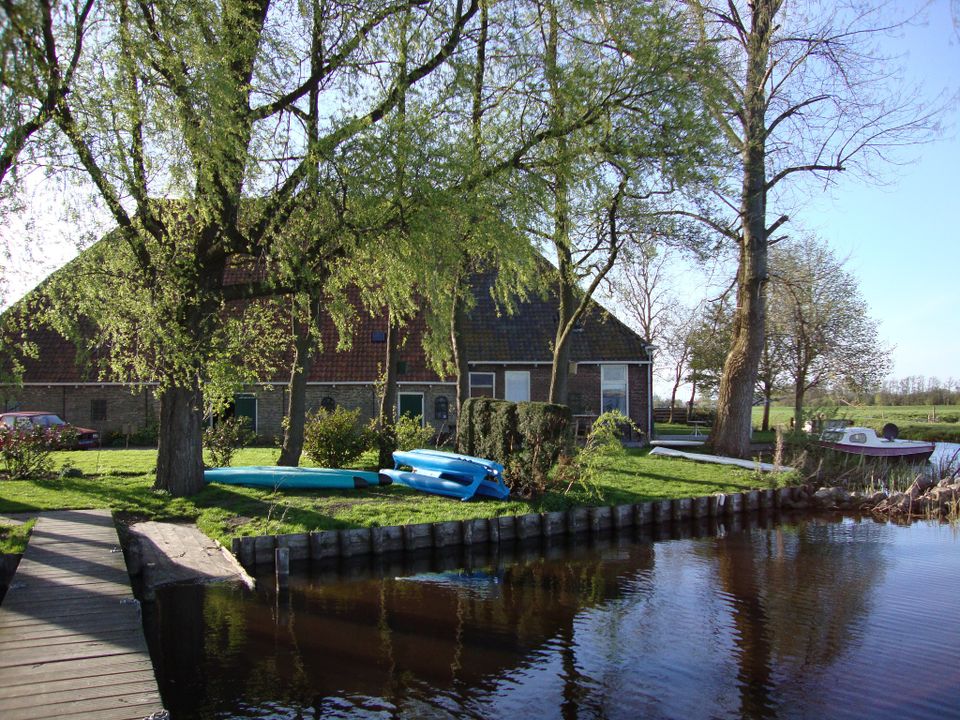 Kampeerboerderij Hettinga in Terherne met op de voorgrond water en twee omgekeerde boten op het gras.