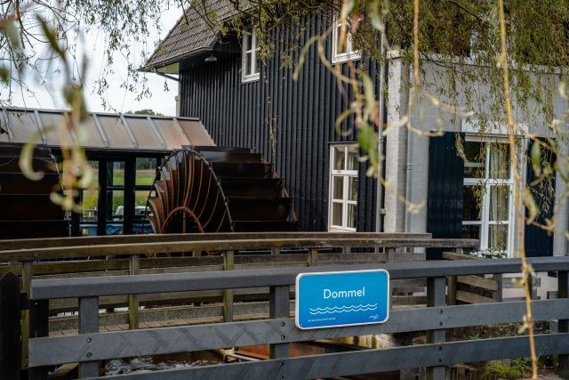 Watermolen langs Het Dommelpad. Een brug met daarop een bordje met 'Dommel'.