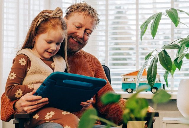 kind bij vader op schoot met een ipad in de hand