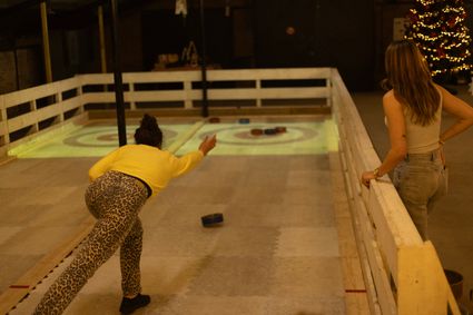 Indoor curlen bij Boerderij De Boerinn in Kamerik, waar twee mensen ontspannen en fanatiek spelen op een verlichte curlingbaan met feestelijke decoratie; actief en gezellig groepsuitje in het Groene Hart.