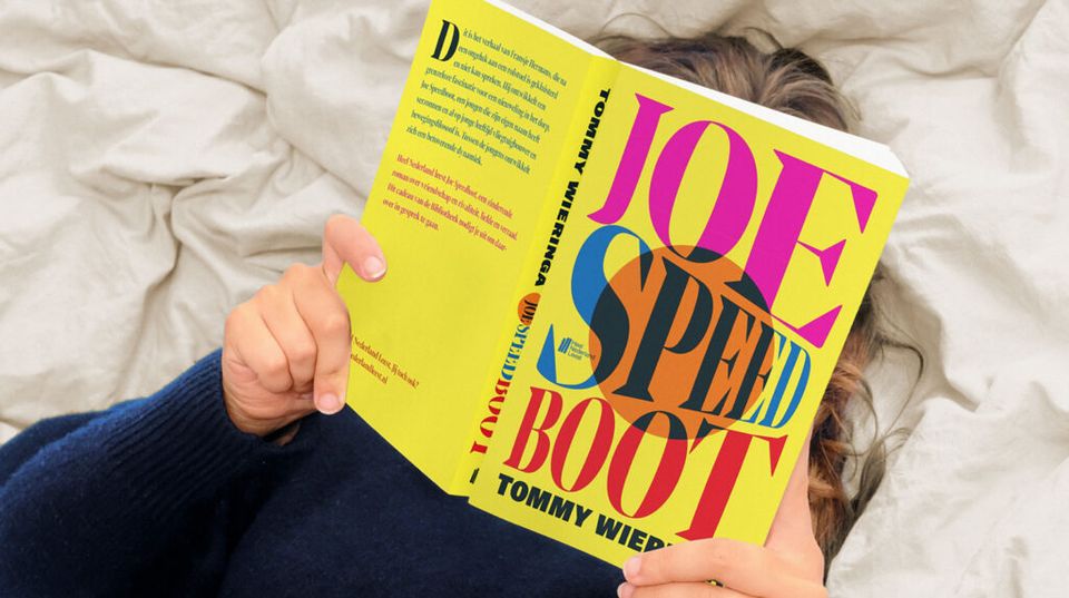 Iemand ligt op bed en heeft het boek Joe Speedboot opengeslagen voor het gezicht