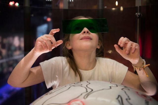 Een meisje ontdekt een nieuwe wereld in het Drents museum. Ze heeft een grote groene plastic bril op dit hoort bij dit interactieve deel van de kindertentoonstelling.