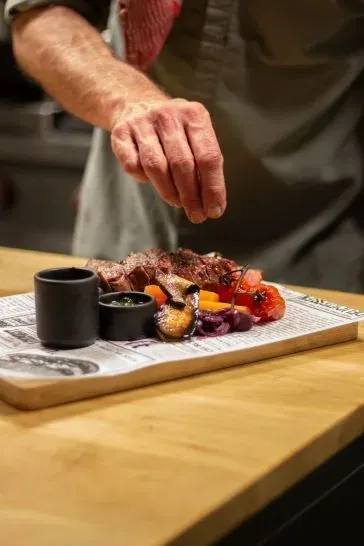 Op de foto zie je de hand van een chef zout strooien over een vleesgerecht.
