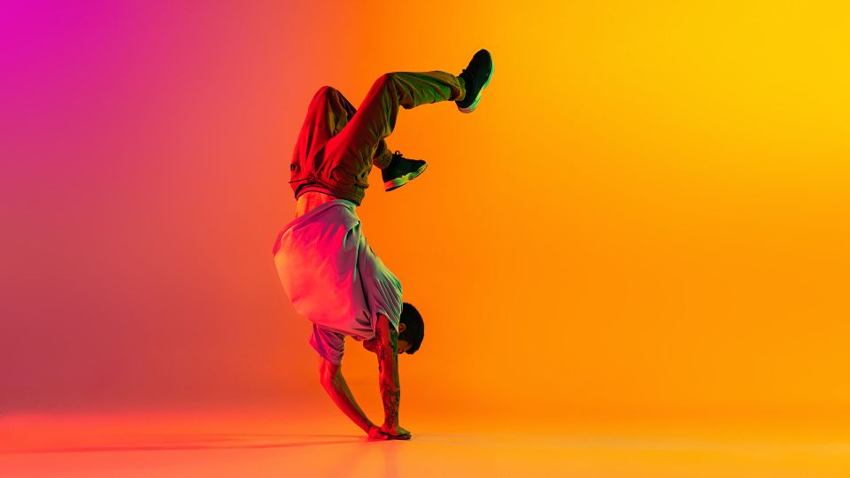 Breakdancer in handstand pose op felgekleurde oranje en roze achtergrond tijdens urban dansoptreden.