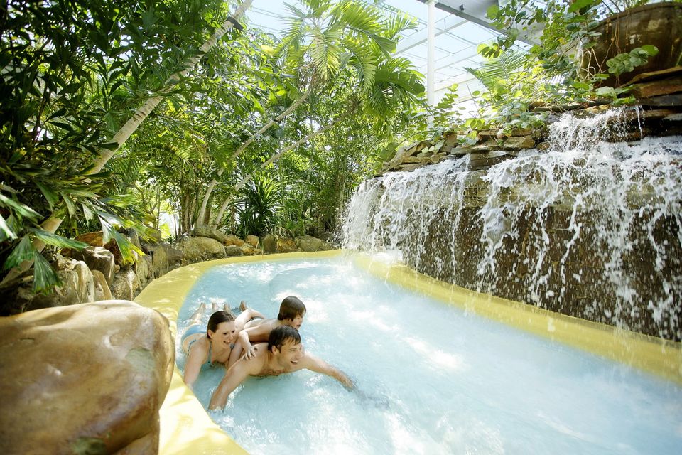 Ouders en kind glijden van de wildwaterbaan in een tropisch zwembad.