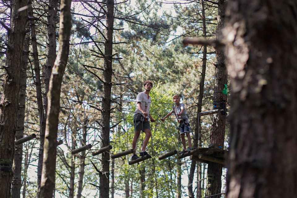 Vader en zoon samen in het klimpark tussen de bomen.