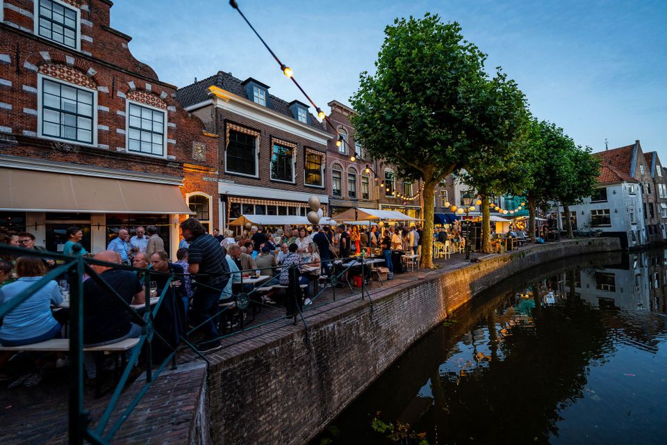 Stedelijk evenement Pracht aan de Gracht in Oudewater, Groene Hart, drukbezochte grachtenkade met terrassen, lichtslingers en historische panden tijdens culinair festival aan het water.