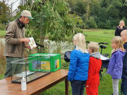 Een gids laat een afbeelding van waterdiertjes zien en 4 kinderen staan er naar te kijken.