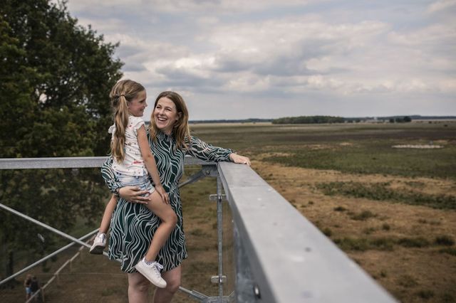 Mutter steht mit ihrer Tochter auf dem Arm oben auf einem Aussichtsturm und schaut in die Natur.