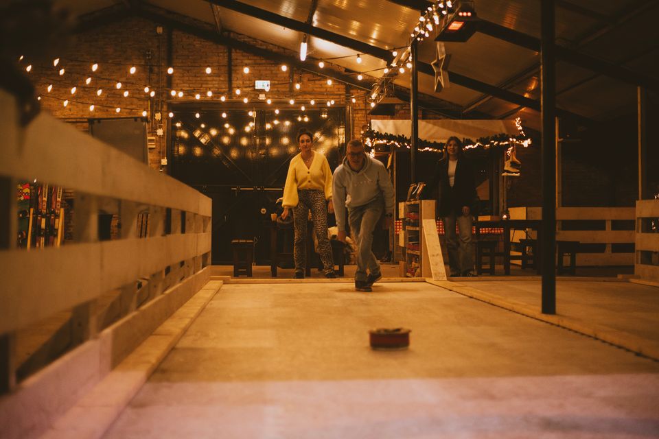 Binnenactiviteit bij Boerderij De Boerinn in Kamerik, waar een groep mensen fanatiek aan het curlen is op een verlichte indoorbaan met warme sfeerverlichting; gezellige en sportieve uitje in het Groene Hart.