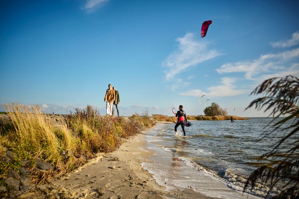 Stel loopt langs het water waar een kitesurfer met kite uit het water loopt.