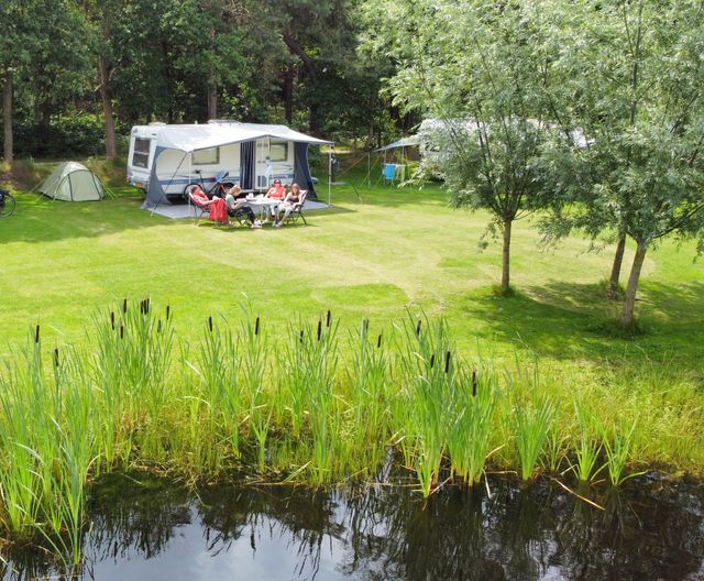 Kampeerplaats van De Gerrithoeve met op de voorgrond een vijver en op de achtergrond caravans op en groen veld met bomen.