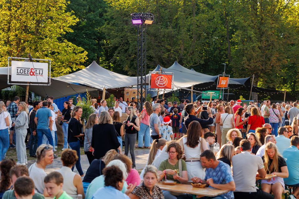 Foodplein van Festival ’t Wonder in Woerden, Groene Hart, met bezoekers bij foodtrucks, bars en terrassen tussen de bomen. Gezellig festivalterrein waar mensen genieten van eten, drinken, lokale horeca en livemuziek tijdens een zomers muziekfestival.