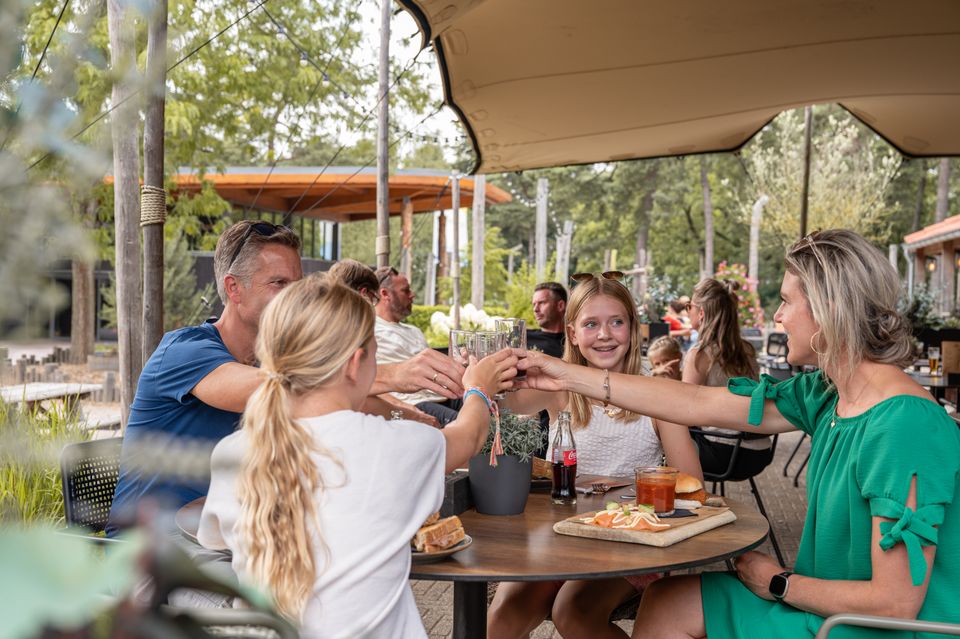 Een familie proost tijdens een lunch op het terras van Brasserie La Forêt bij RCN Het Grote Bos in Doorn. De foto laat de gezellige en gastvrije sfeer van het vakantiepark op de Utrechtse Heuvelrug zien.