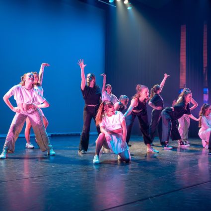 Dansers in kleurige kleding in actie op een podium.
