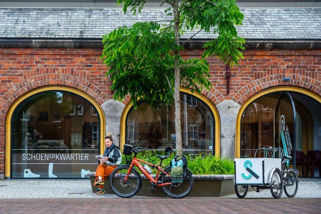 Een vrouw, lezend op een bankje voor museum het Schoenenkwartier.