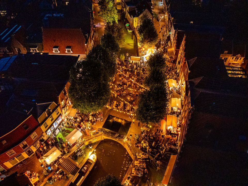 Evenement Pracht aan de Gracht in Oudewater, Groene Hart. Verlichte terrassen, historische binnenstad en bezoekers langs de gracht tijdens een sfeervol stadsfestival, gezien vanuit de lucht in de avond boven het centrum van Oudewater.