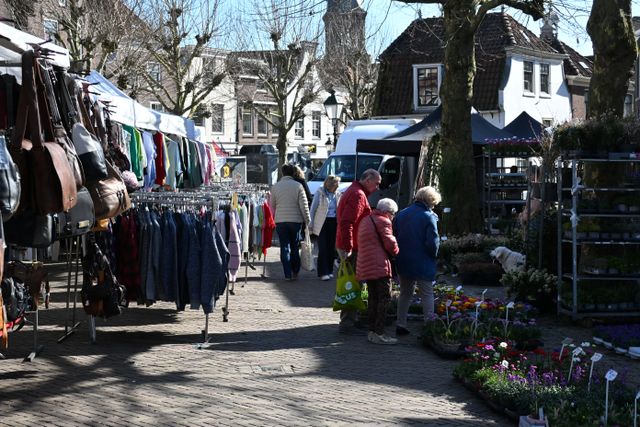 Stadscentrum weekmarkt met kramen en winkelend publiek in Oudewater, Groene Hart, historische straat met bakstenen gevels en lokale marktproducten.  Weekmarkt met kledingkramen en bloemenverkoop in Oudewater, Groene Hart.