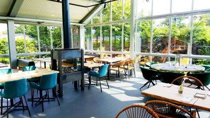 Inrichting van restaurant Polderhuis, gelegen in een glazen kas met fluwelen en rieten stoelen, vierkante en ronde tafels en een open haard.