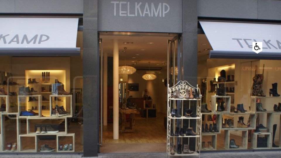 Speciaalzaak Telkamp Schoenen Woerden, provincie Utrecht, Groene Hart, entree van de schoenenwinkel in het centrum met verlichte etalages, houten presentatiemeubels en collectie dames- en herenschoenen.