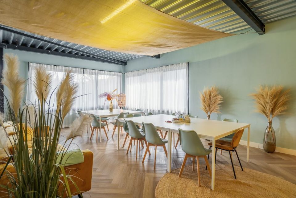 Een blauwe ruimte met geel doek aan het plafond en witte tafel met stoelen eromheen.