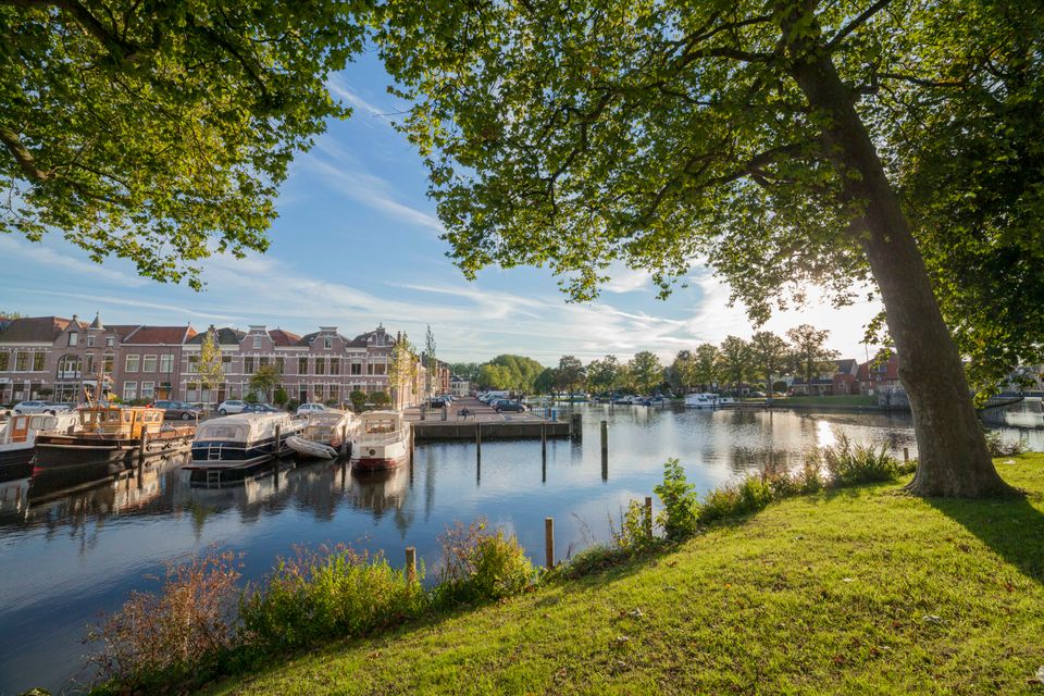 Zicht op de haven van Woerden met aangemeerde boten, historische gevels en groene bomen op een zonnige dag – een rustgevende plek om te ontspannen tijdens een bezoek aan Woerden.