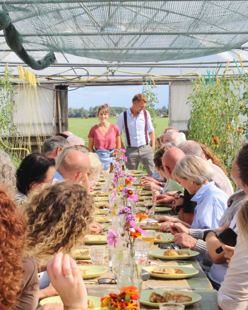 Een lange culinaire tafel met mensen en chefkok's Koekoek en de Waard.