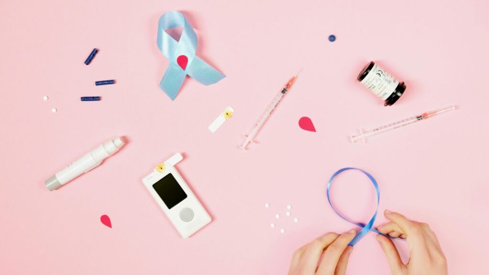 Pillendoosjes, injectiespuiten, een blauwe ribbon, een epipen en een glucosemeter op een roze achtergrond