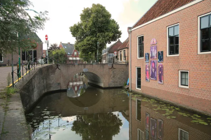 Historische gracht met bakstenen boogbrug bij het Gerard David Buitenmuseum in Oudewater, Utrechtse Waarden, Groene Hart, met muurschilderingen van schilder Gerard David op de gevel en weerspiegeling in het water van de binnenstad.