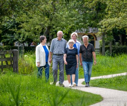 Vrijwilligers van Logeerhuis Bredius wandelen samen over een groen pad in het Brediuspark in Woerden, omringd door natuur en bomen.