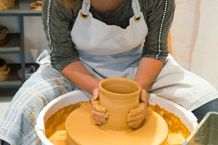 Creatieve workshop potten bakken Kunst op de Hoek, Woerden, Groene Hart, cursist vormt klei op draaischijf tijdens keramiek workshop met handen in natte klei en ambachtelijk handwerk in atelier.
