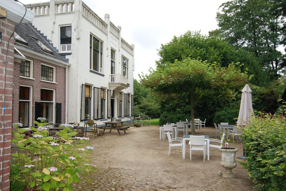 Ein stattliches Gebäude in Drenthe mit einer Terrasse daneben, auf der weiße Stühle und Tische stehen.