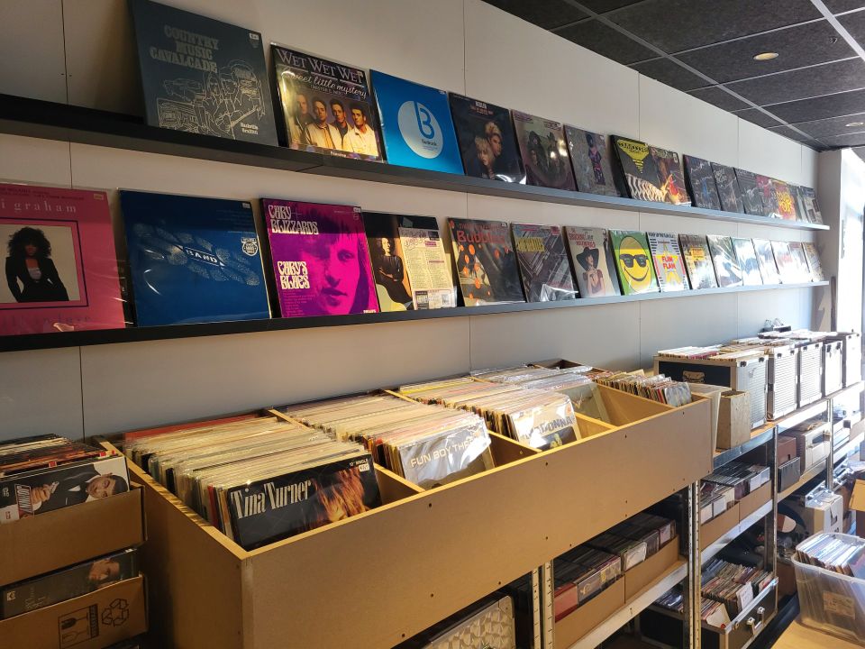Muziekwinkel HiFi Stereo in Woerden, Groene Hart, interieur met lange wand vol vinylplaten en bakken met lp’s, overzicht van platenzaak met muziekcollectie en albumhoezen.