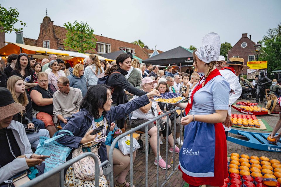 Een vrouw in klederdracht die kaas uitdeelt n op de avondkaasmarkt in Edam