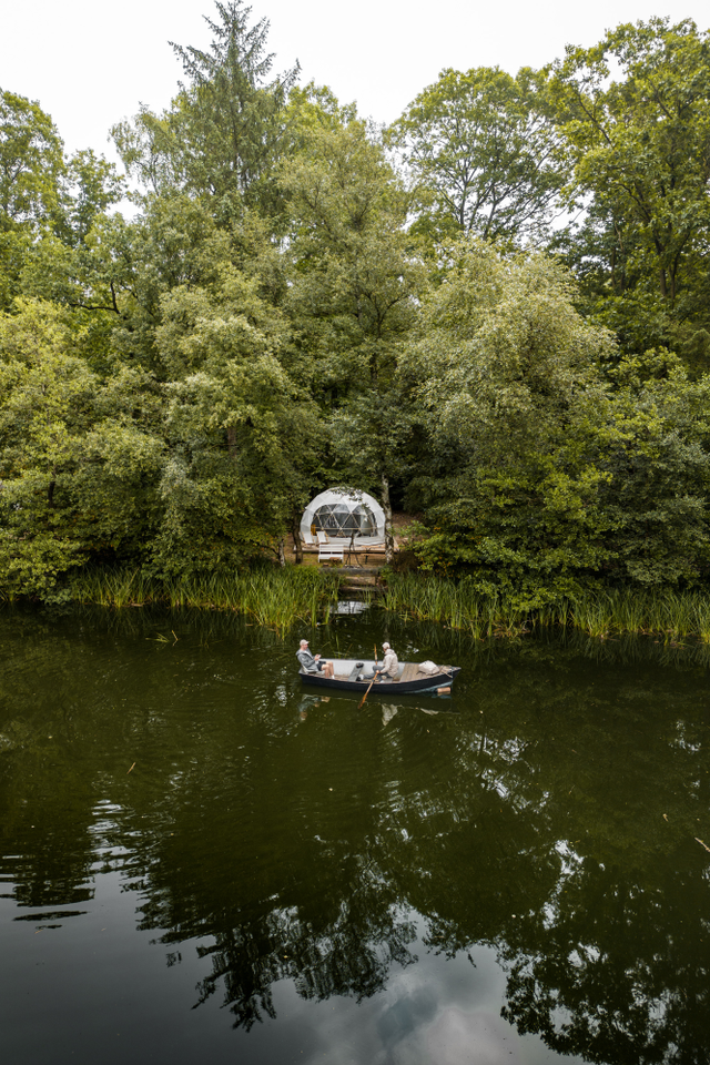 Twee mensen varen met het roeibootje op het meertje bij hun Dome-accommodatie op Landgoed Mariahoeve.