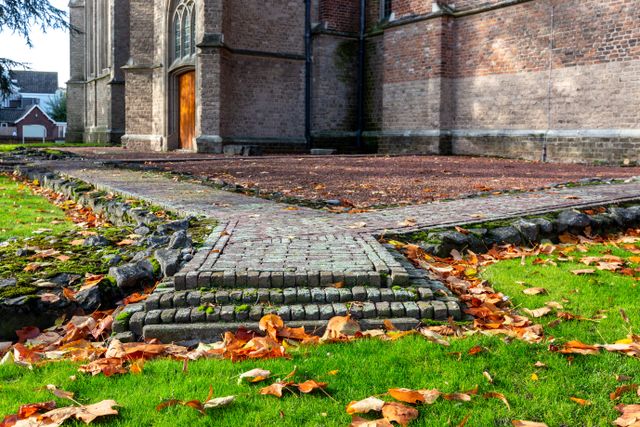 Herfstbladeren liggen in het gras. Uit het gras komen de bakstenen contouren van een tempel. de kerk op de achtergrond.